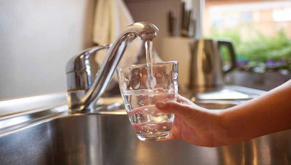 hands pouring glass of fresh water from tap in kitchen