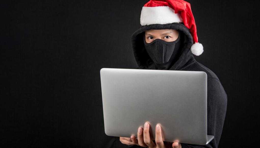 Mysterious male santa hacker holding laptop computer, anonymous man on black background, ransomware cyber attack and internet security on Christmas holiday concepts