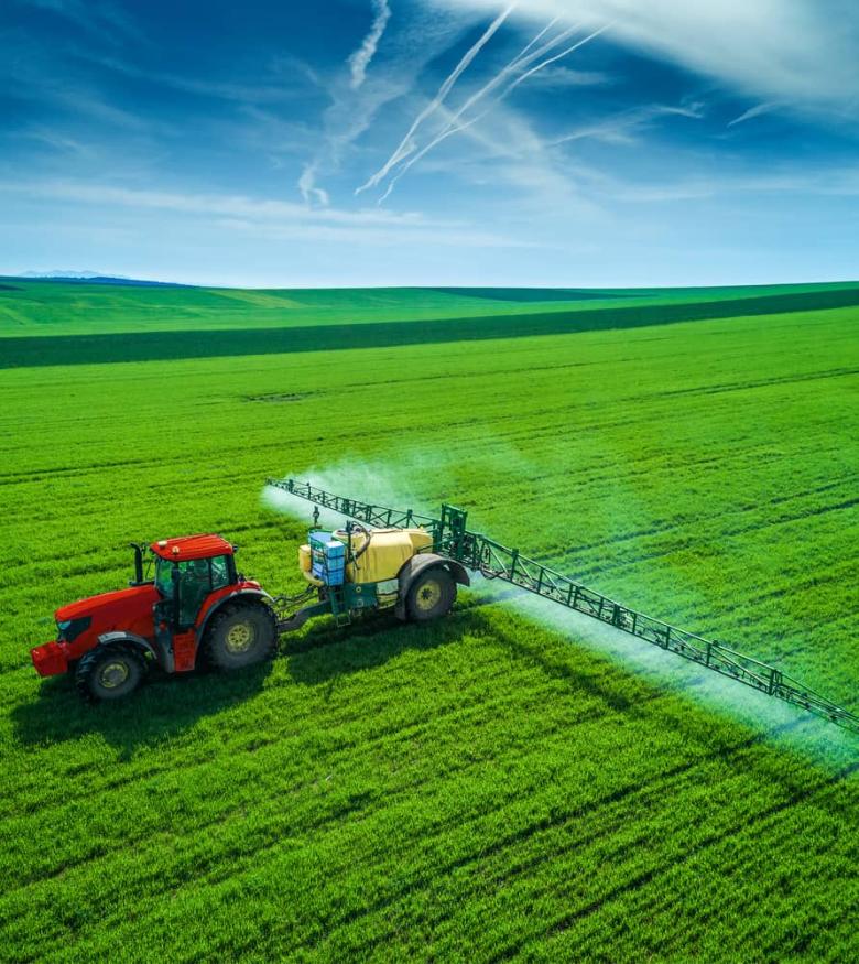 Aerial view of farming tractor plowing and spraying on field.