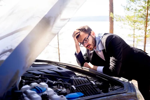 Stressed businessman looking at car engine breakdown