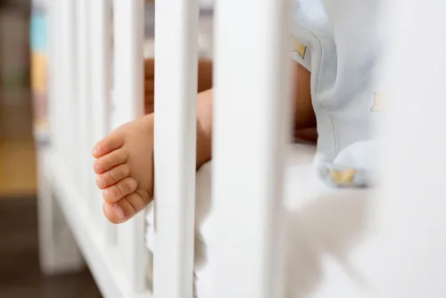 Close-up of a baby's foot sticking out between white crib slats