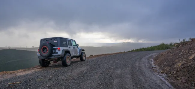 Four-wheel drive SUV on a gravel road in a mountainous area with overcast skies.