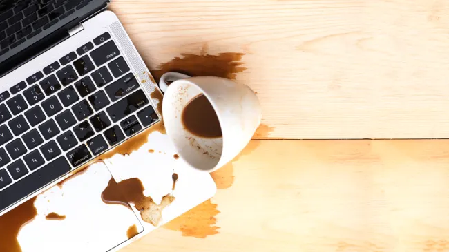 Spilled coffee on a laptop keyboard on a wooden desk