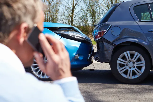 Man on phone after a car accident with visible damage to both cars.