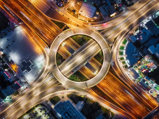 Aerial view of a busy roundabout with multiple intersecting highways at night, illustrating common car accident hotspots