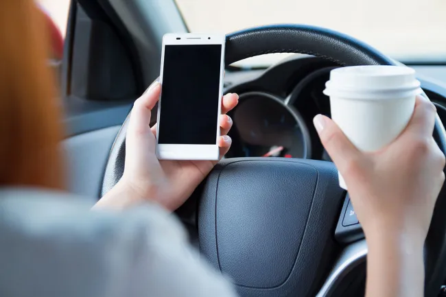 What is Tennessee Doing to Combat the Rise of Distracted Driving? - A man in a car with a cup of coffee and mobile phone